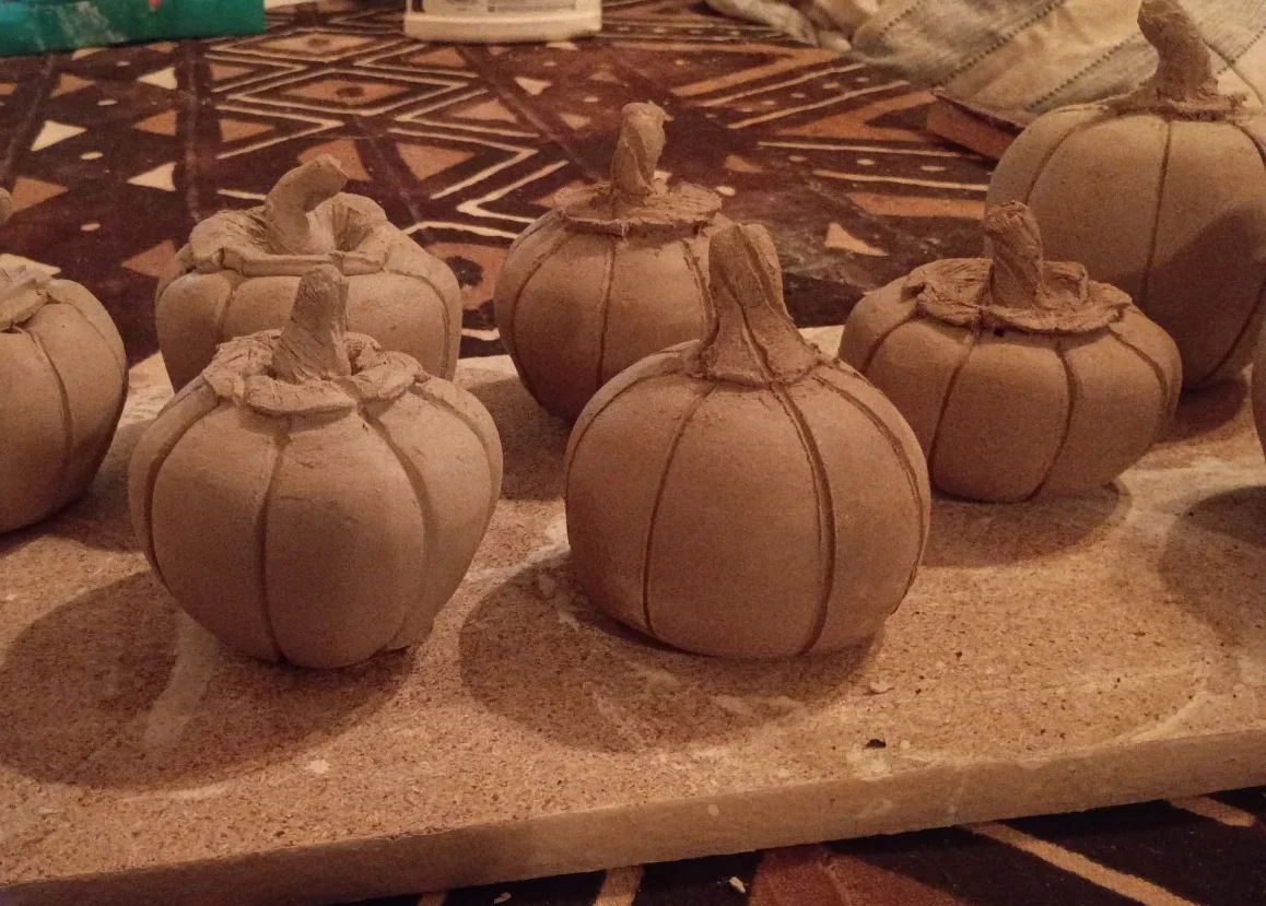 Unfired clay pumpkins on a board
